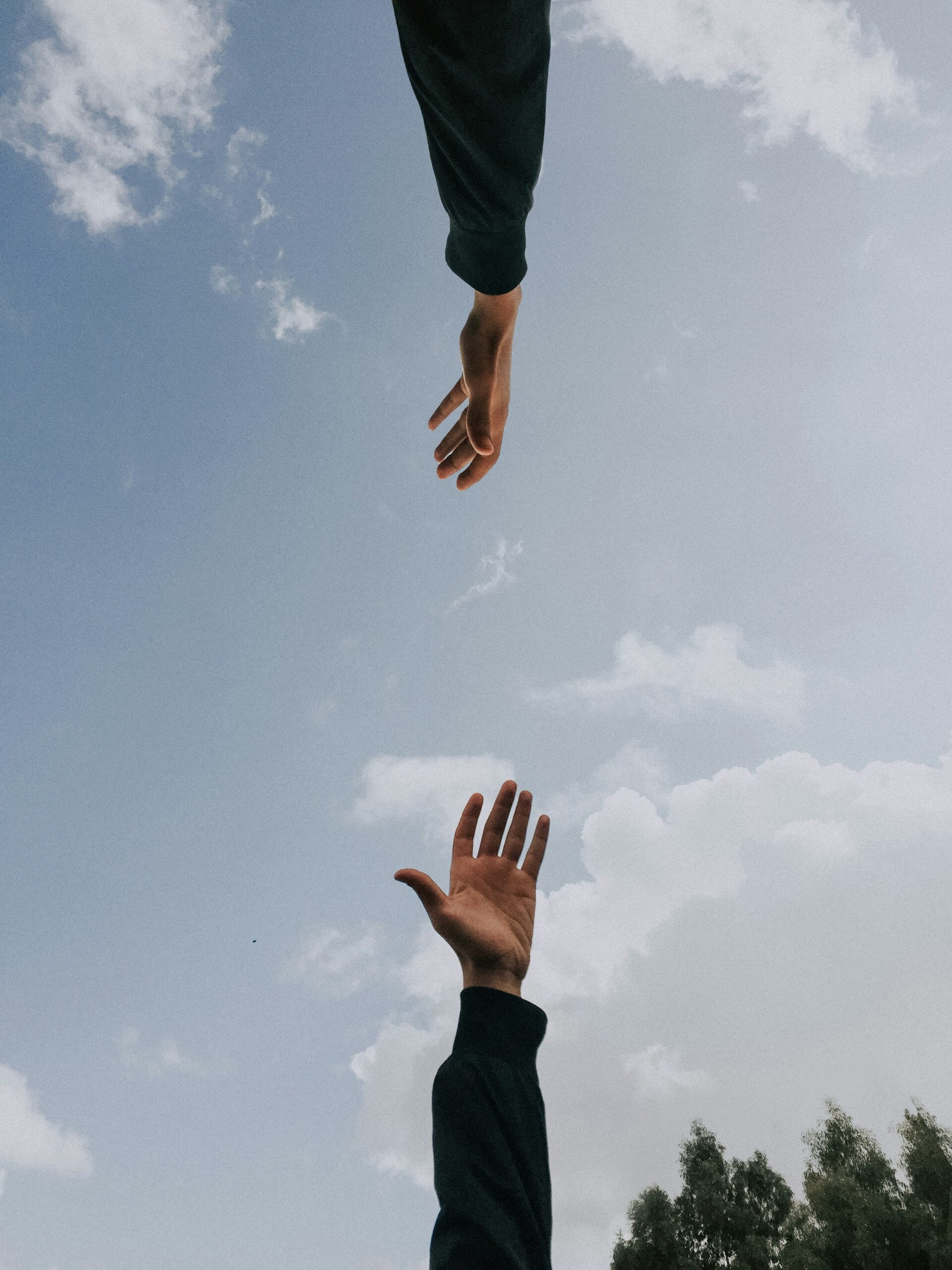 Two hands reaching toward each other against a cloudy sky, symbolizing support and connection.
