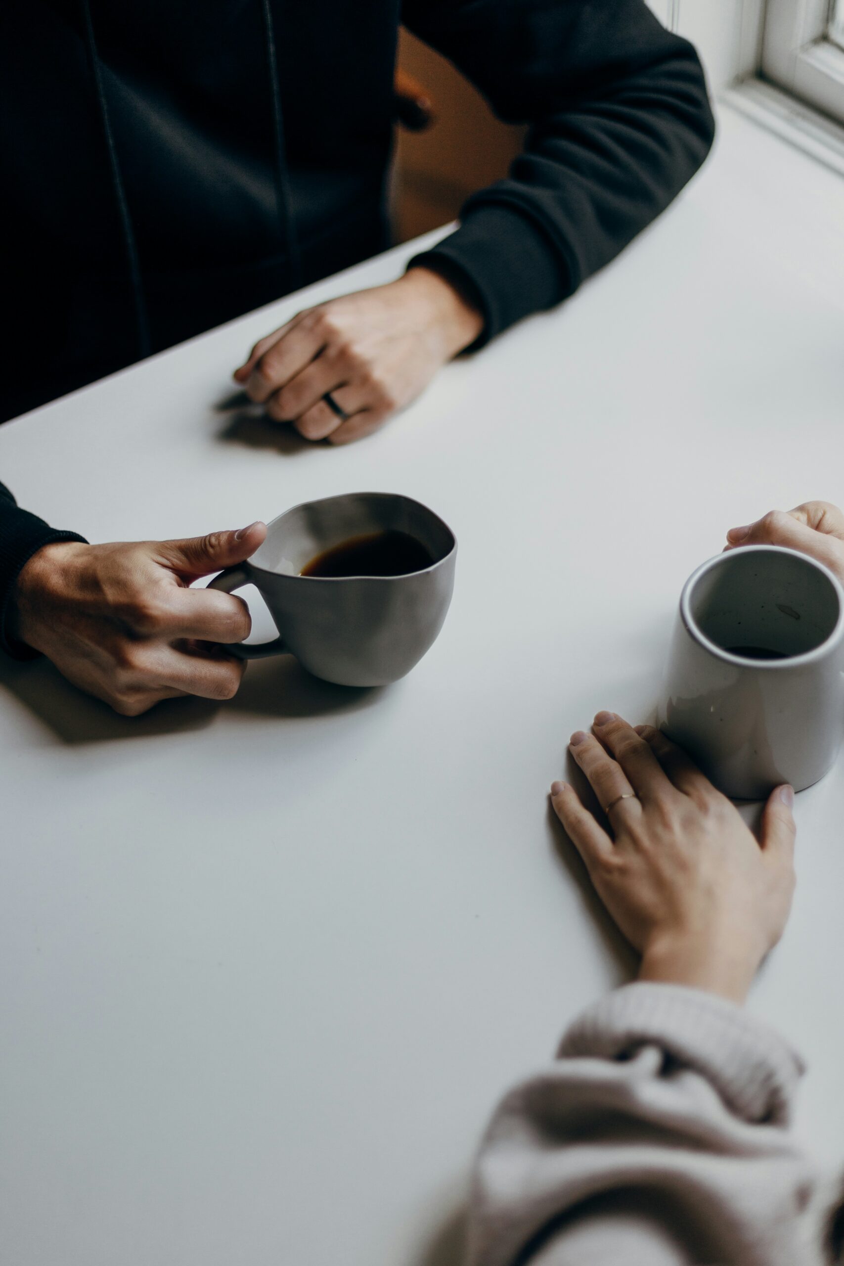 Two people holding warm drinks at a table, sharing a calm and supportive conversation.